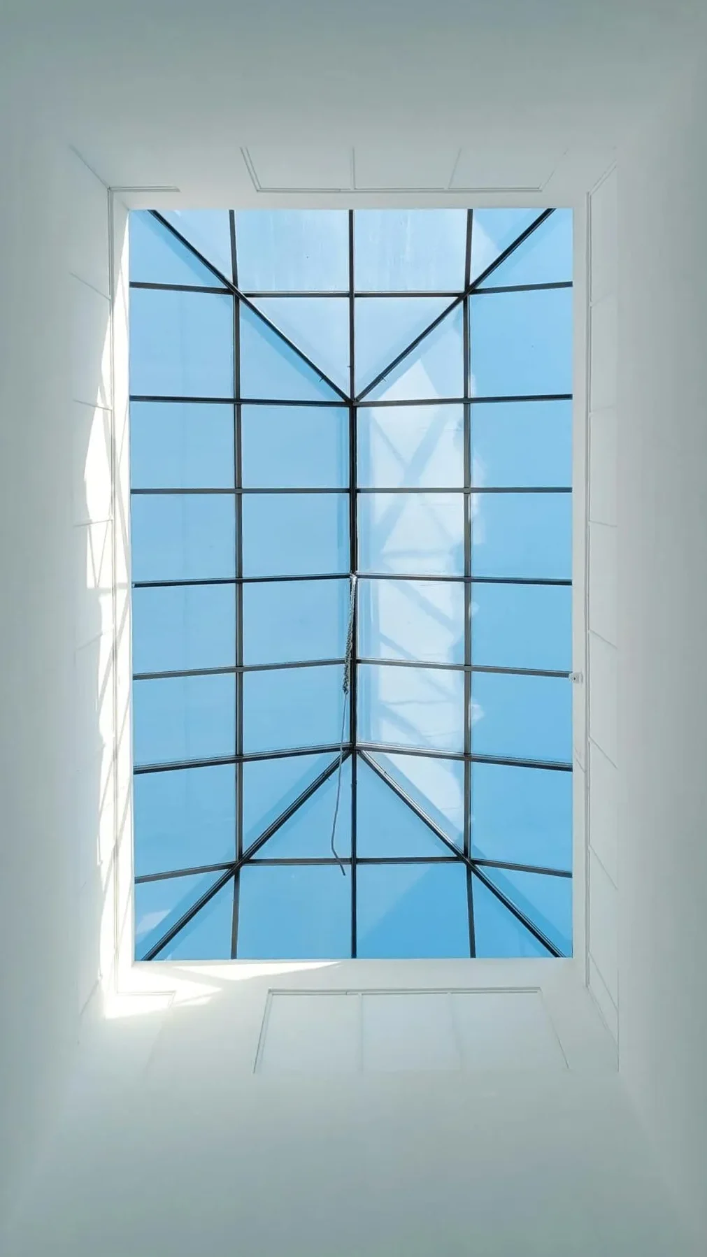 View of a glass ceiling skylight with a geometric grid pattern framing a clear blue sky, creating a sense of openness and tranquility. How to Stop Skylight Condensation.