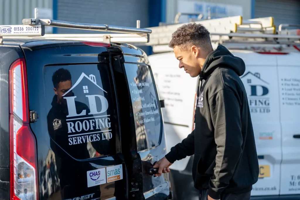 A man in a black hoodie stands by a van with "LD Roofing Services Ltd" logo. He's opening the back door. Another similar van is in the background.