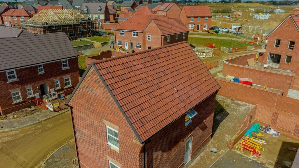 Aerial view of a housing development with red brick houses at various construction stages. The area is active, conveying a sense of progress.